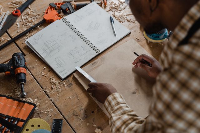 Woodworker sketching project plans in workshop with tools and materials on a wooden table.